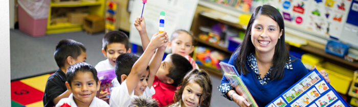 Teacher in classroom surrounded by elementary students.