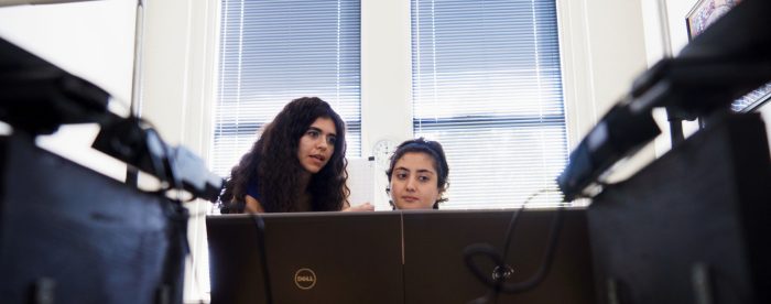 Two females, one is teaching the other about something on the computer.