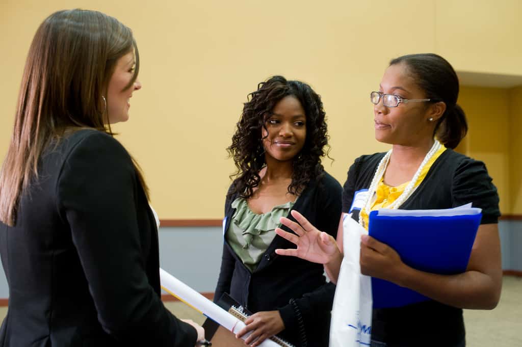 Three woman speaking about something. They are all dressed professionally. 