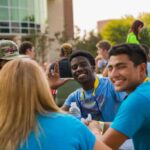 Group of students siting at table outside smiling at the camera.