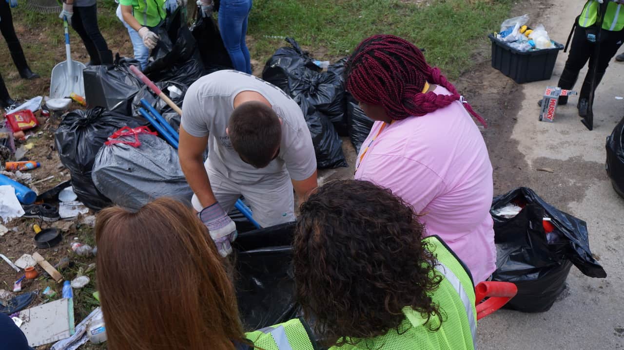 Four individuals looking at the garbage with the garbages in the bag.
