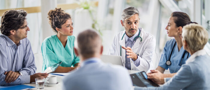 Male doctor and his female colleagues talking to team of business people on a meeting in the hospital.