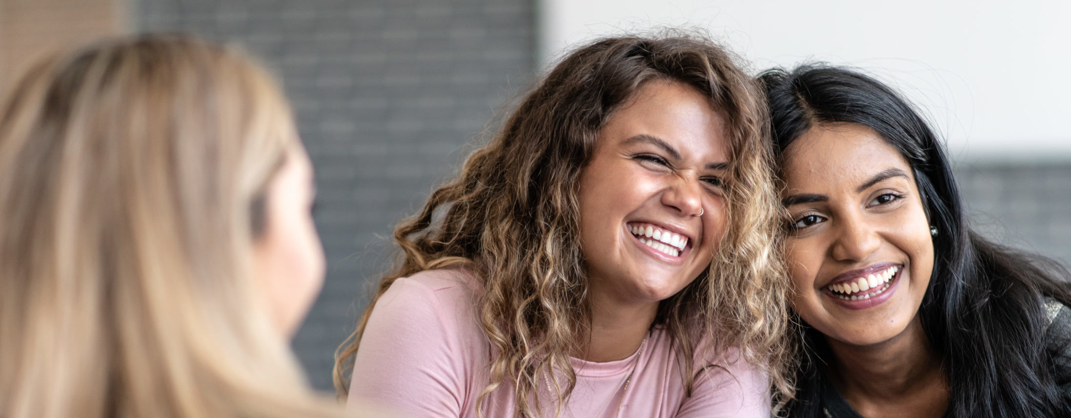 group therapy session. One is of African decent and the other is of Indian decent. Bother are dressed casually and are sitting among their multi-ethnic peers with smiles on their faces.