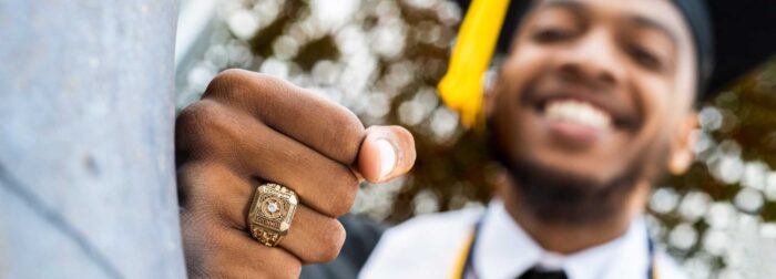 Graduating student with cap and gown on and the class ring on his finger.