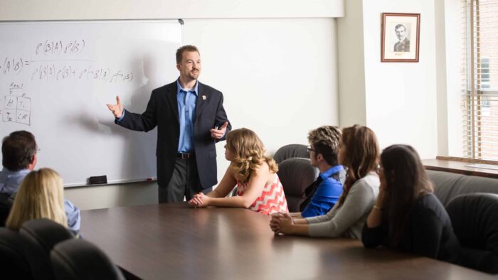 Psychology instructor teaching class around a large boardroom table.