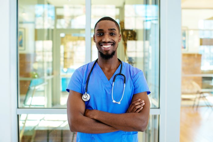 Portrait of a friendly male nurse wearing blue scrubs uniform and stethoscope, with arms crossed in hospital
