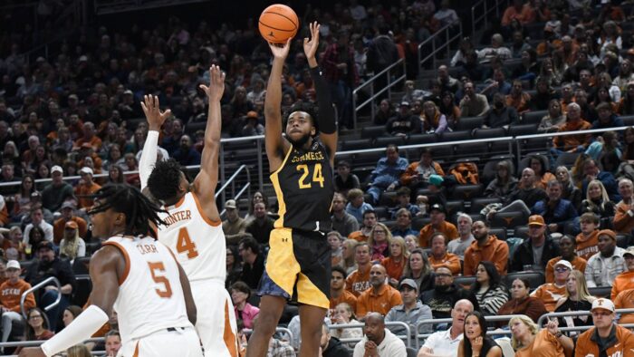 Player jumps to shoot the basketball ball while a second player blocks.