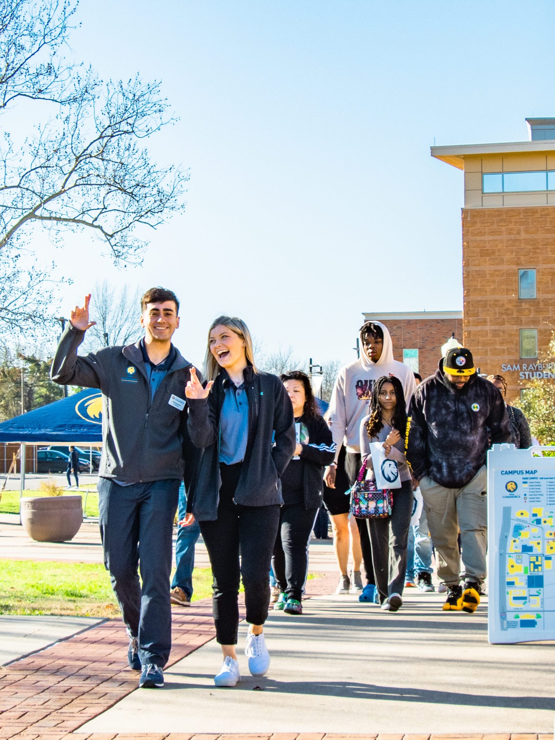 A group of student walking through the campus. The front two are giving the lion's sign and the ones in the back are looking around.