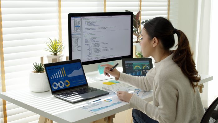 Asia young business woman sit busy at home office desk work code on desktop PC reskill upskill for job career remote self test IT deep tech ai design skill online html text for cyber security.