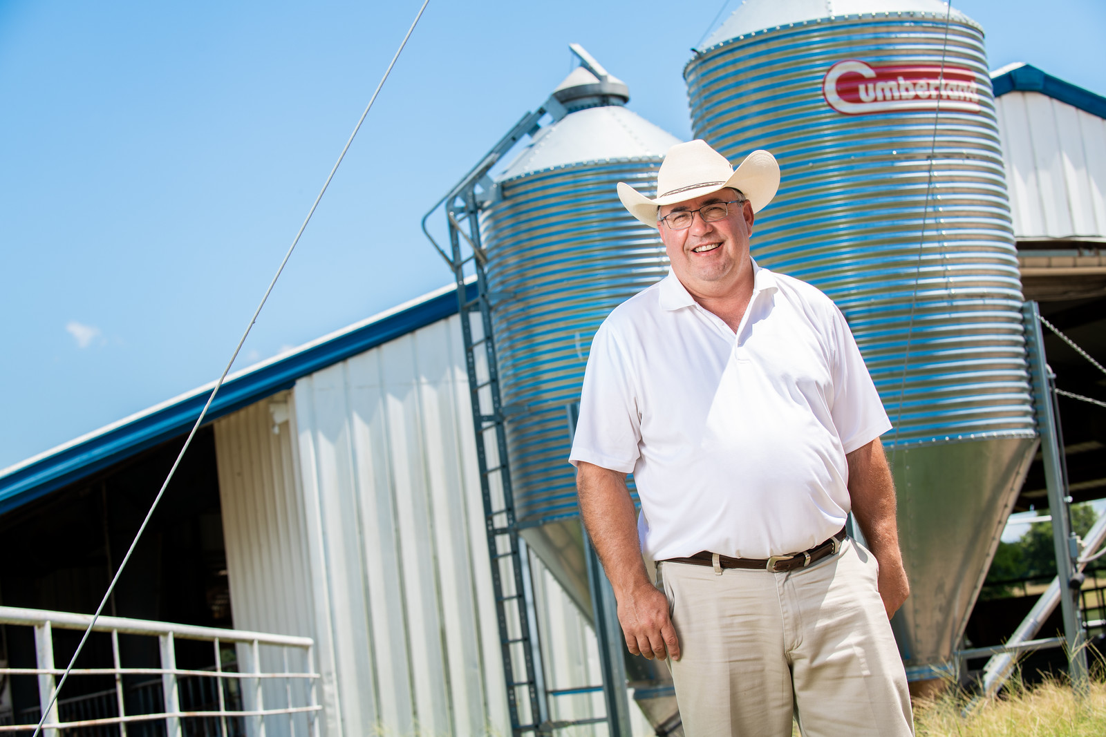 An older male wearing a hat in front of a farming factility.