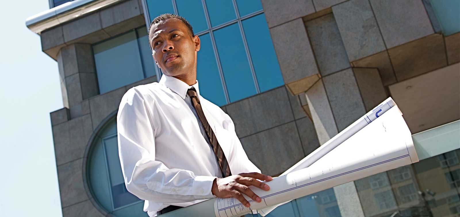 An African male in front of a construction building with blue prints. 