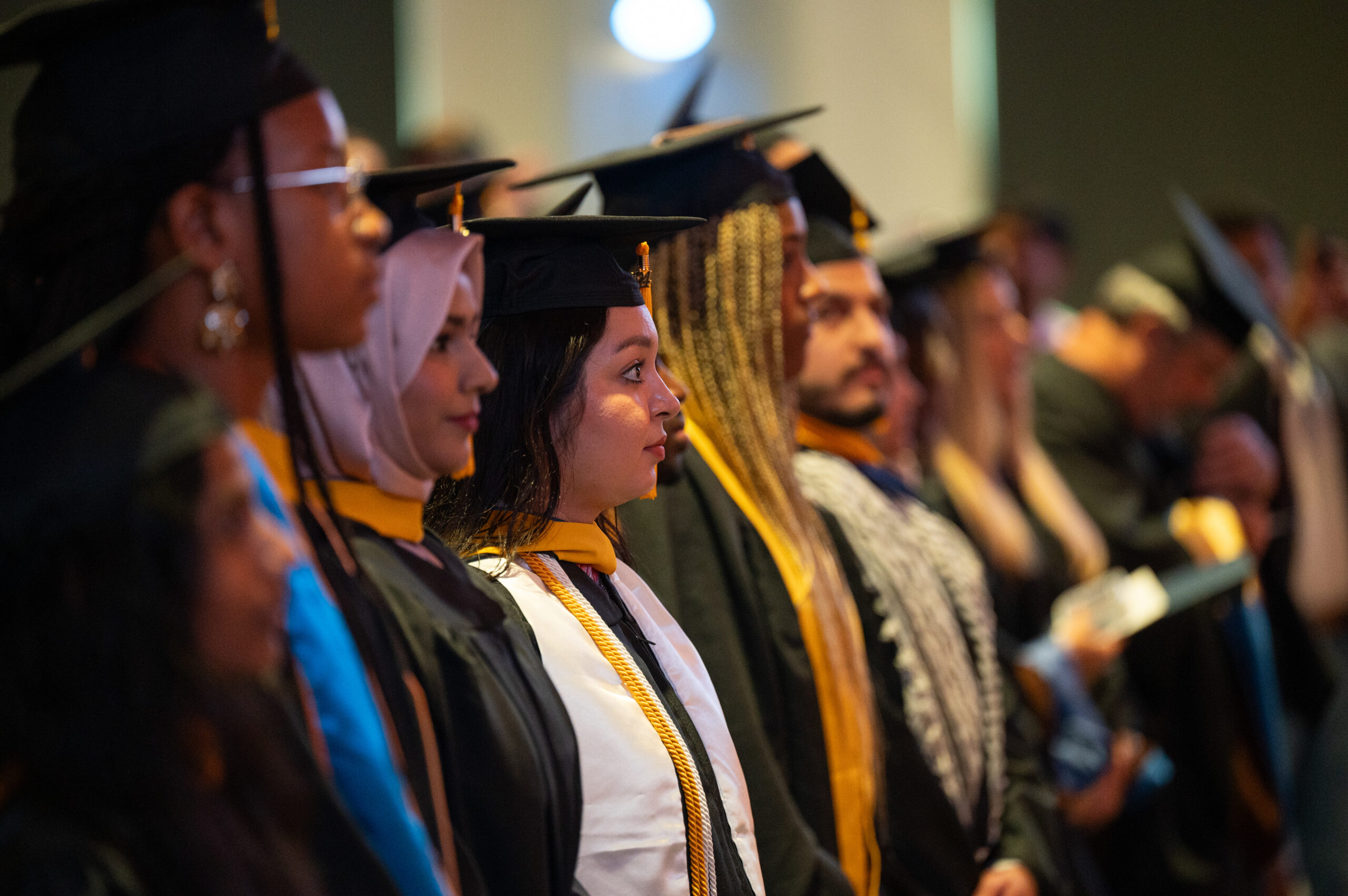 A group of graduate student lined up. There is a focus on a female looking to the right.