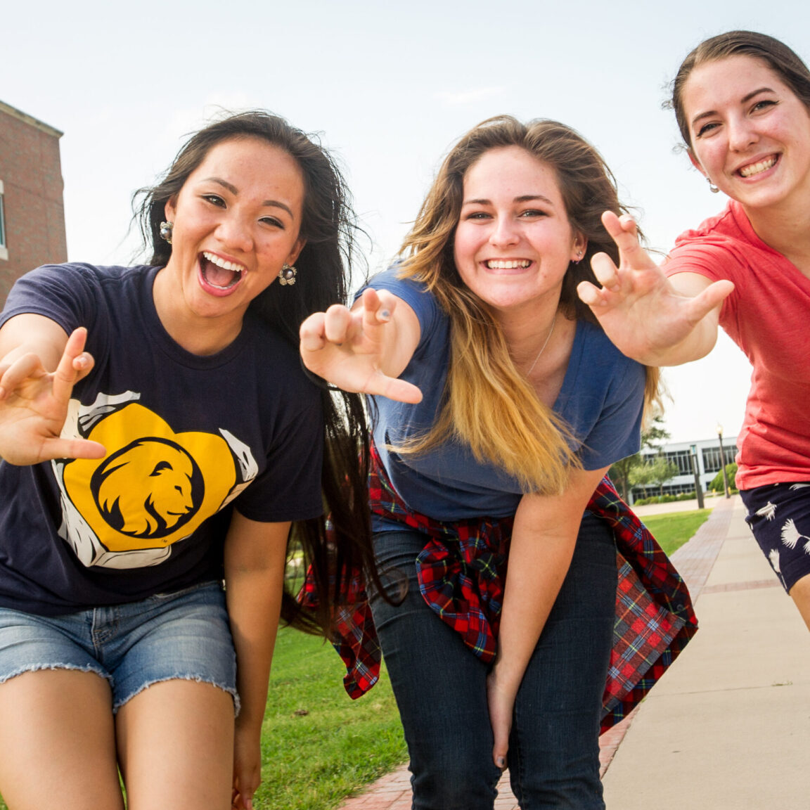 Three female students smiling while showing the leo hand sign.