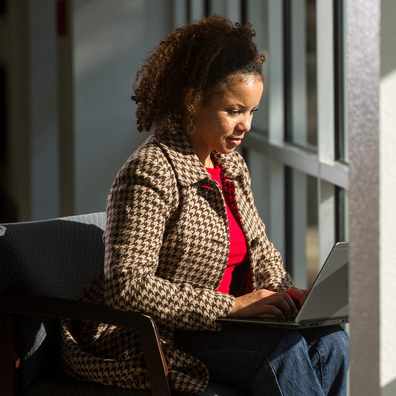 Woman working on a computer sitting by windows.