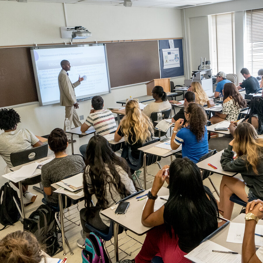 A group of university students in class while a male professor lectures.