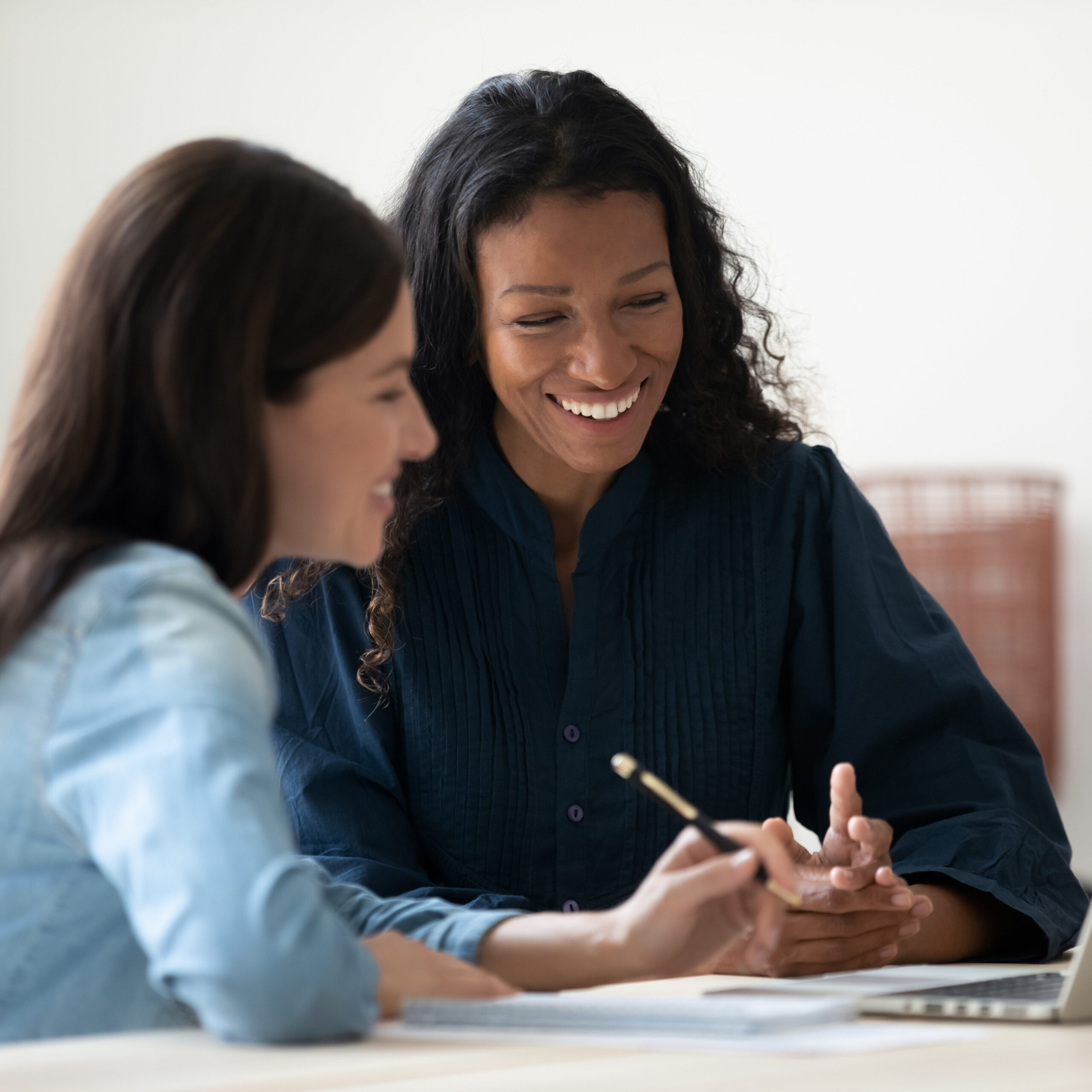 Close up happy young businesswoman using laptop with laughing female mentor