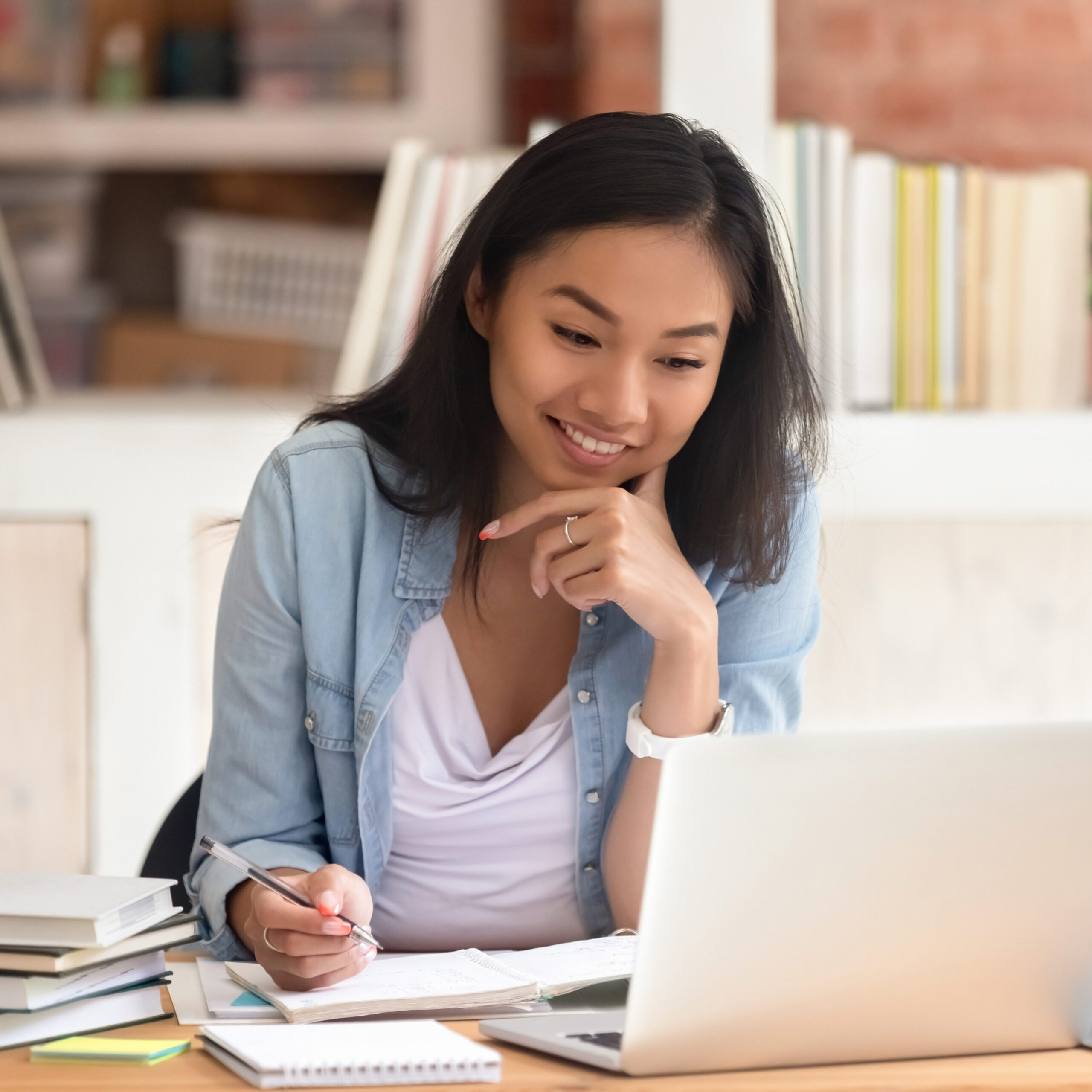 Smiling asian girl student study in library with laptop books.