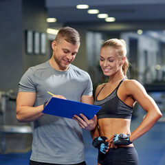 smiling young woman with personal trainer in gym