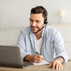 New knowledge online at home. Young man in headphones making notes and looking at laptop computer in living room