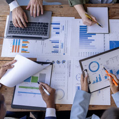 Group of confident business people point to graphs and charts to analyze market data, balance sheet, account, net profit to plan new sales strategies to increase production capacity.