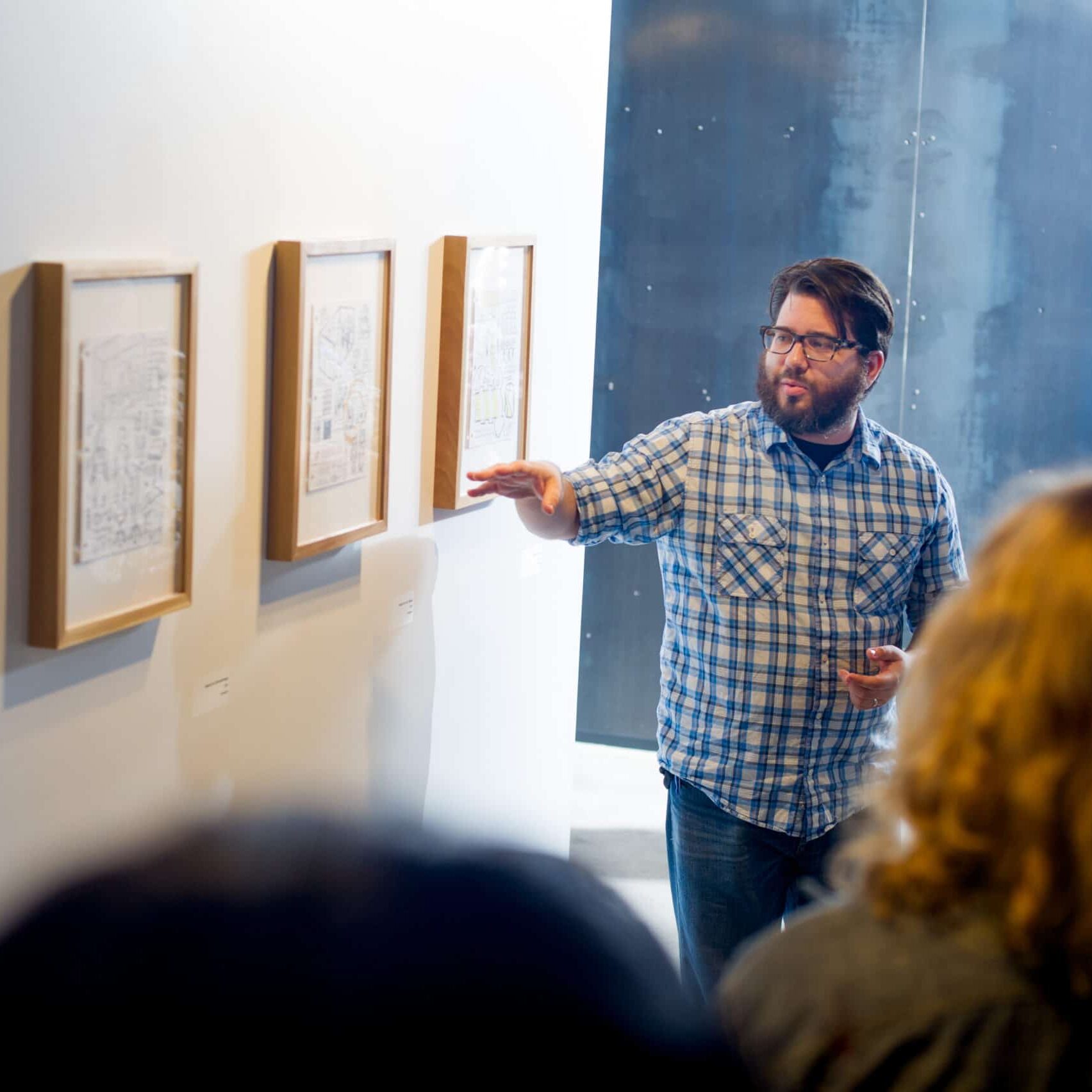 Man presenting three pieces of hanging art.