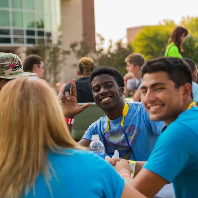 Group of students siting at table outside smiling at the camera.
