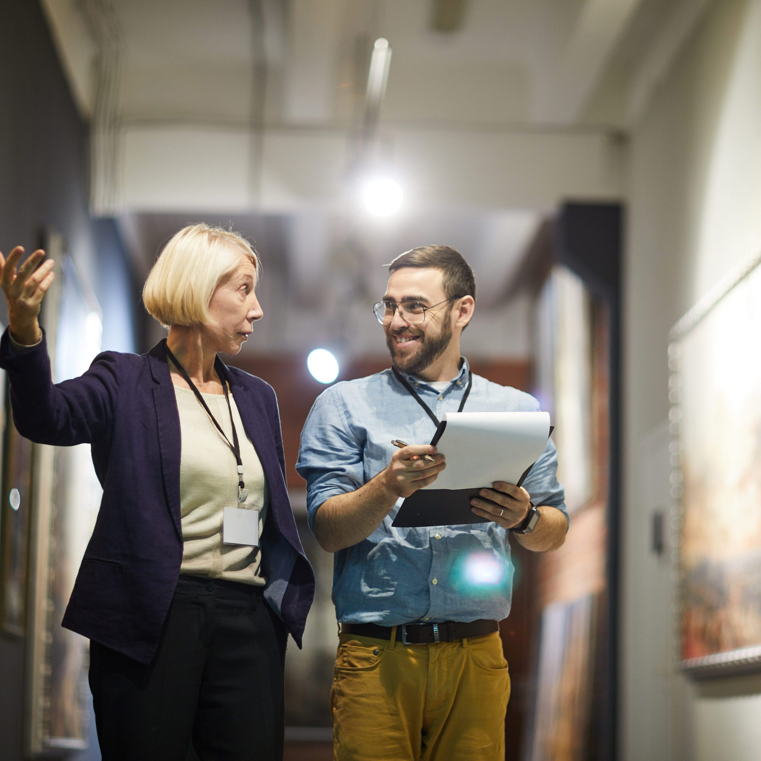 Portrait of two cheerful museum workers discussing paintings walking in art gallery, copy space.