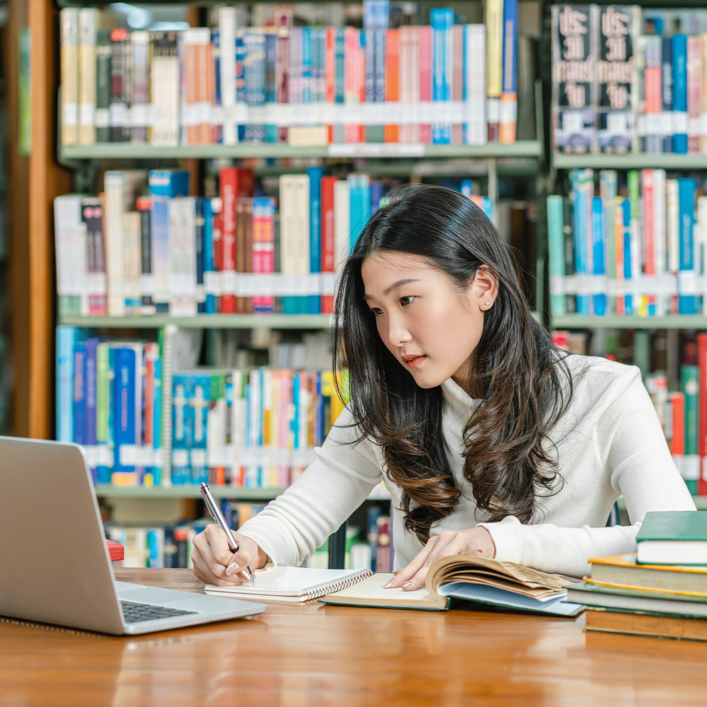 A female at the library on the computer studying with books in front of her.