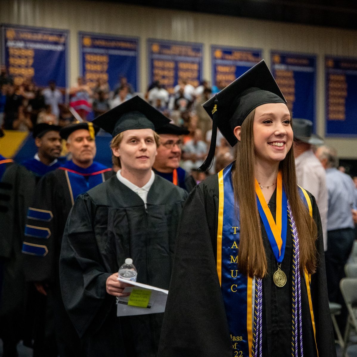 A female student smiling while walking down the aisle during graduating