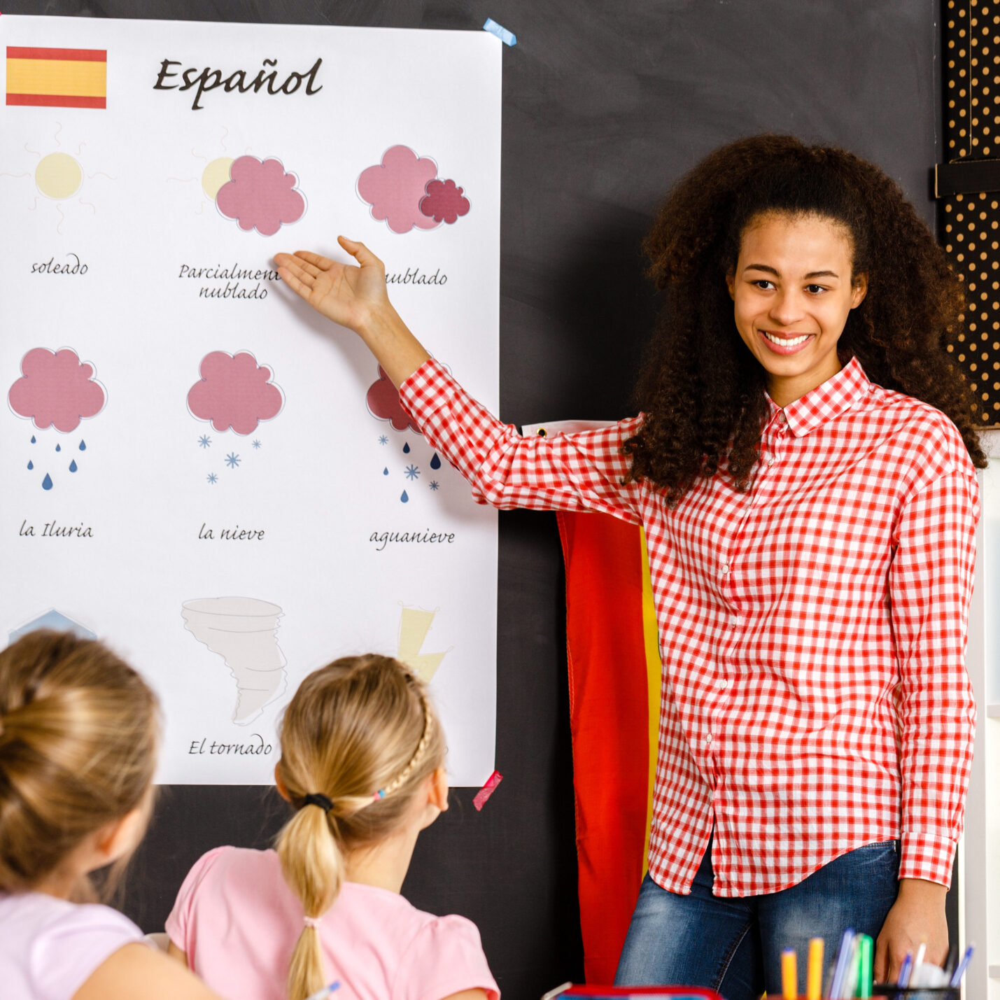An instructor uses a chart to teach Spanish to young students in a classroom.
