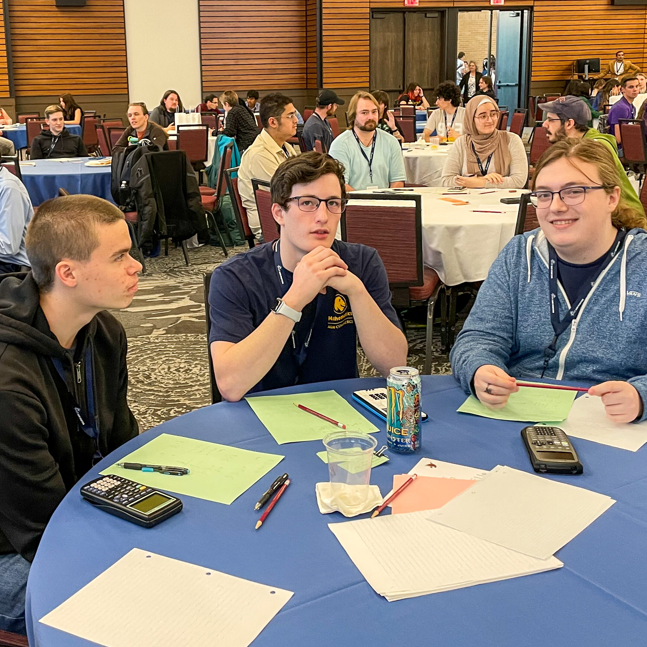 Three students sit at a table with calculators, paper and pencils.