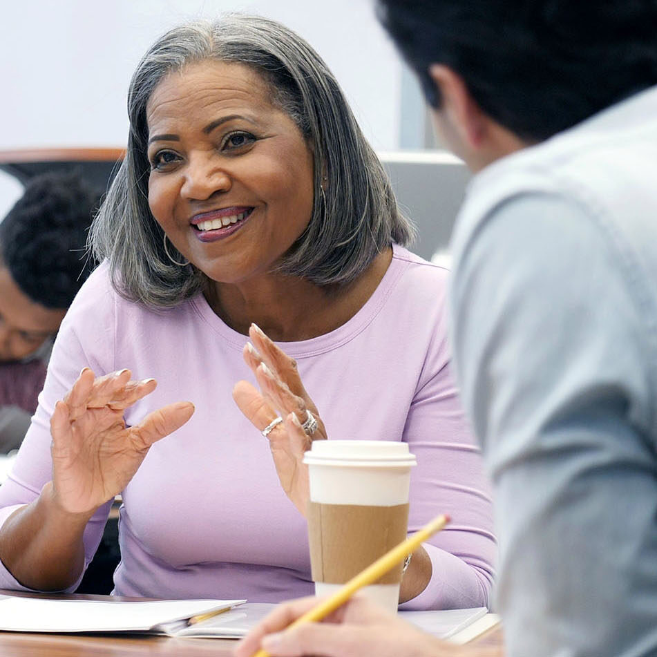 Beautiful mature African American female college student gestures as she discusses something during a study group session with classmates.