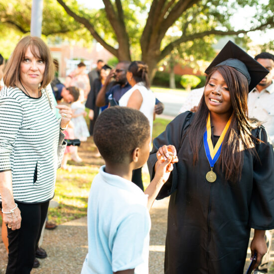 A graduating mother touching her son's hand.