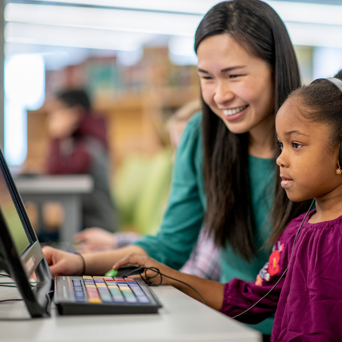 An enfant girl using an assistive technology computer with a teacher assisted beside her.