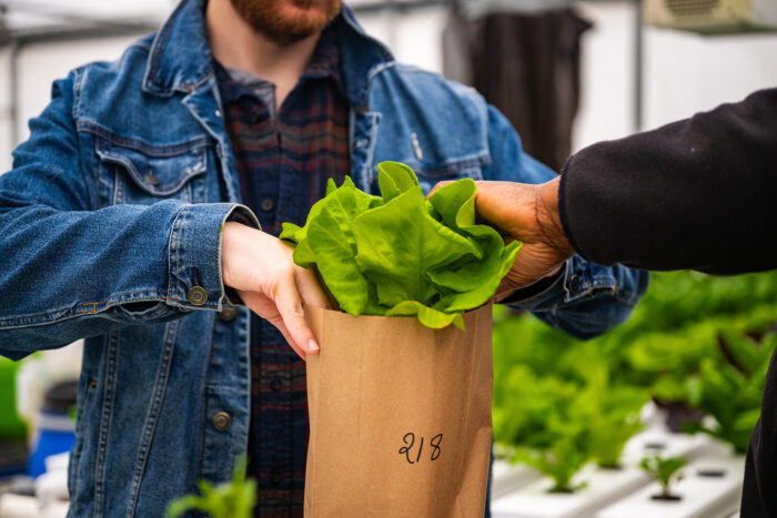Someone placing lettuce into a brown paper bag with a student.