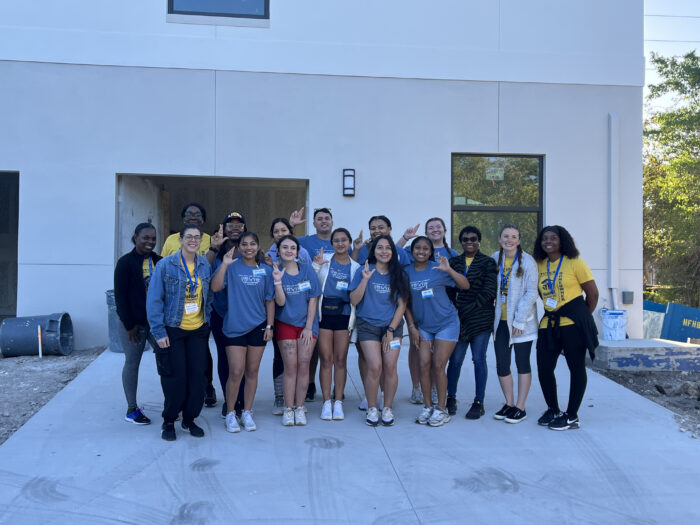 A large group of people pose for a photo in the driveway of a modern home.