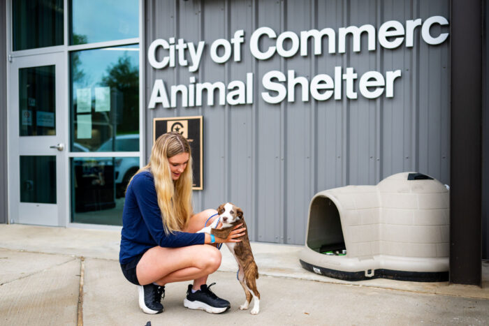 Young woman volunteering with a small puppy in front of the City of Commerce Animal Shelter