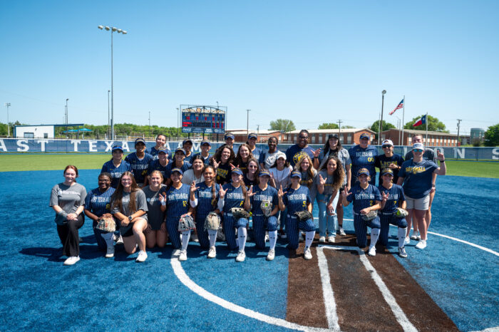 A college softball team poses on the field for a team photo.