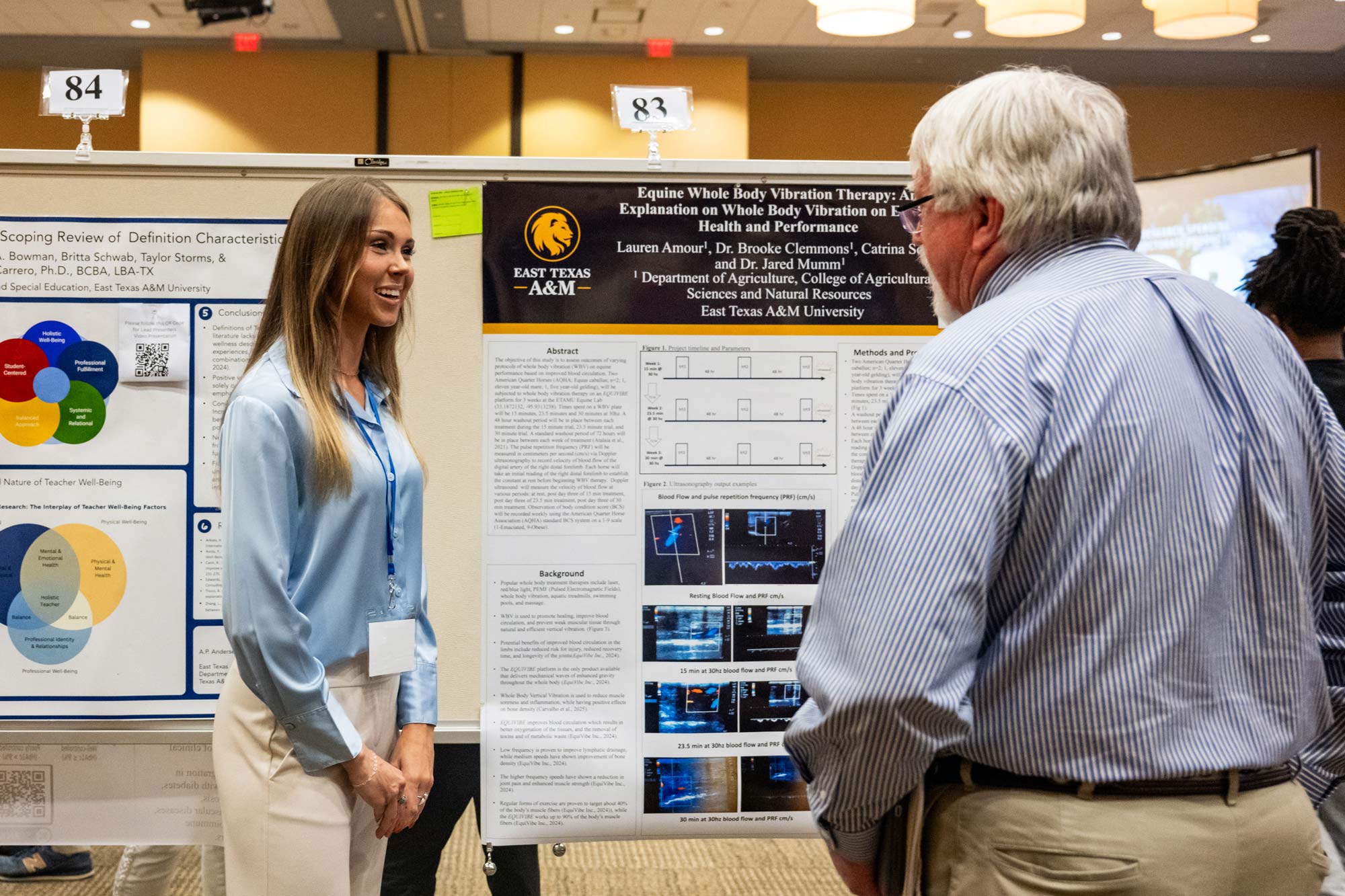 Two people smile and talk. Posters with research are displayed in the background.