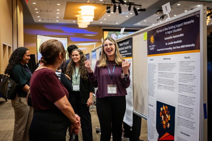 Several people stand in front of poster boards featuring research projects. The people are smile and talk.