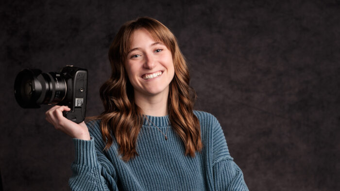 A headshot photo of a person posing while holding a camera. A photo of Morgan Gridley, future NASA intern.