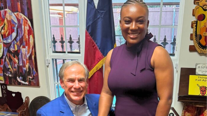 Two people posing for a photo while shaking hands. the person on the left is seated in a wheelchair while the person on the right is standing.
