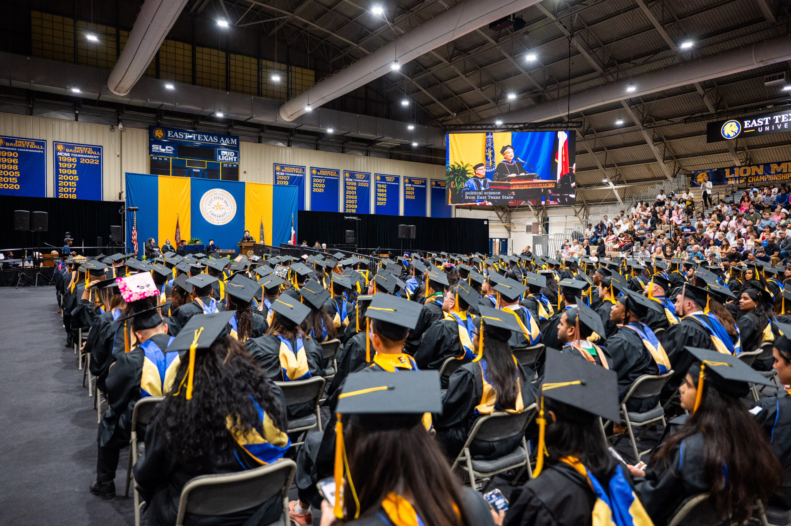 A large crowd of college graduates during a graduation ceremony inside of a gymnasium.