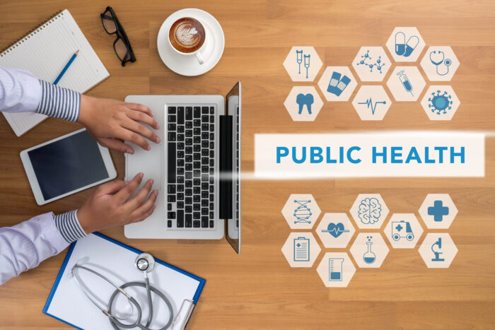 A work desk with hands typing on a laptop, with the words 'Public Health' featured.