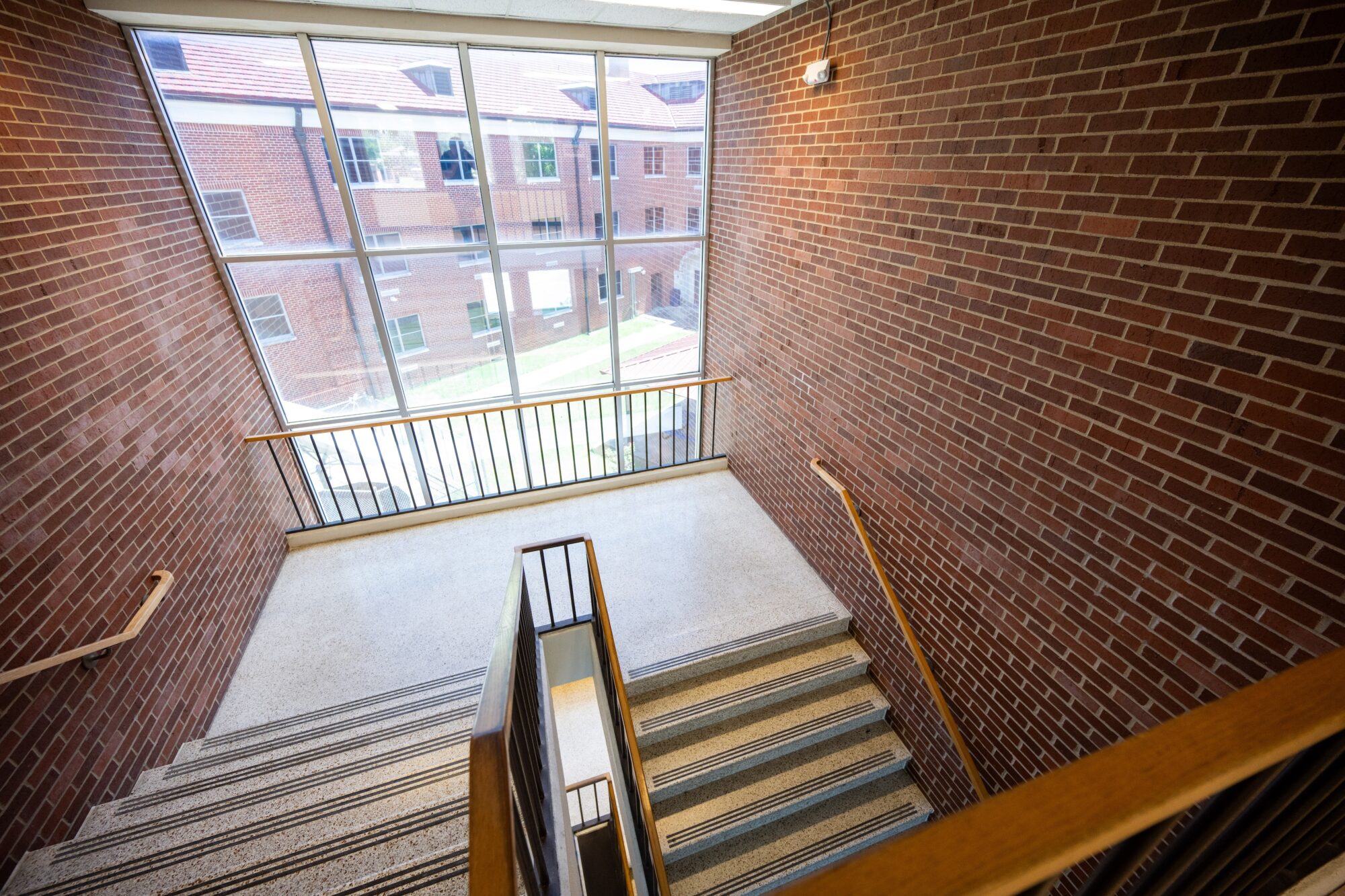 Photo taken on the stairway from the upper-floor interior balcony. A large window in the stairwell provides a view of the outdoor courtyard.