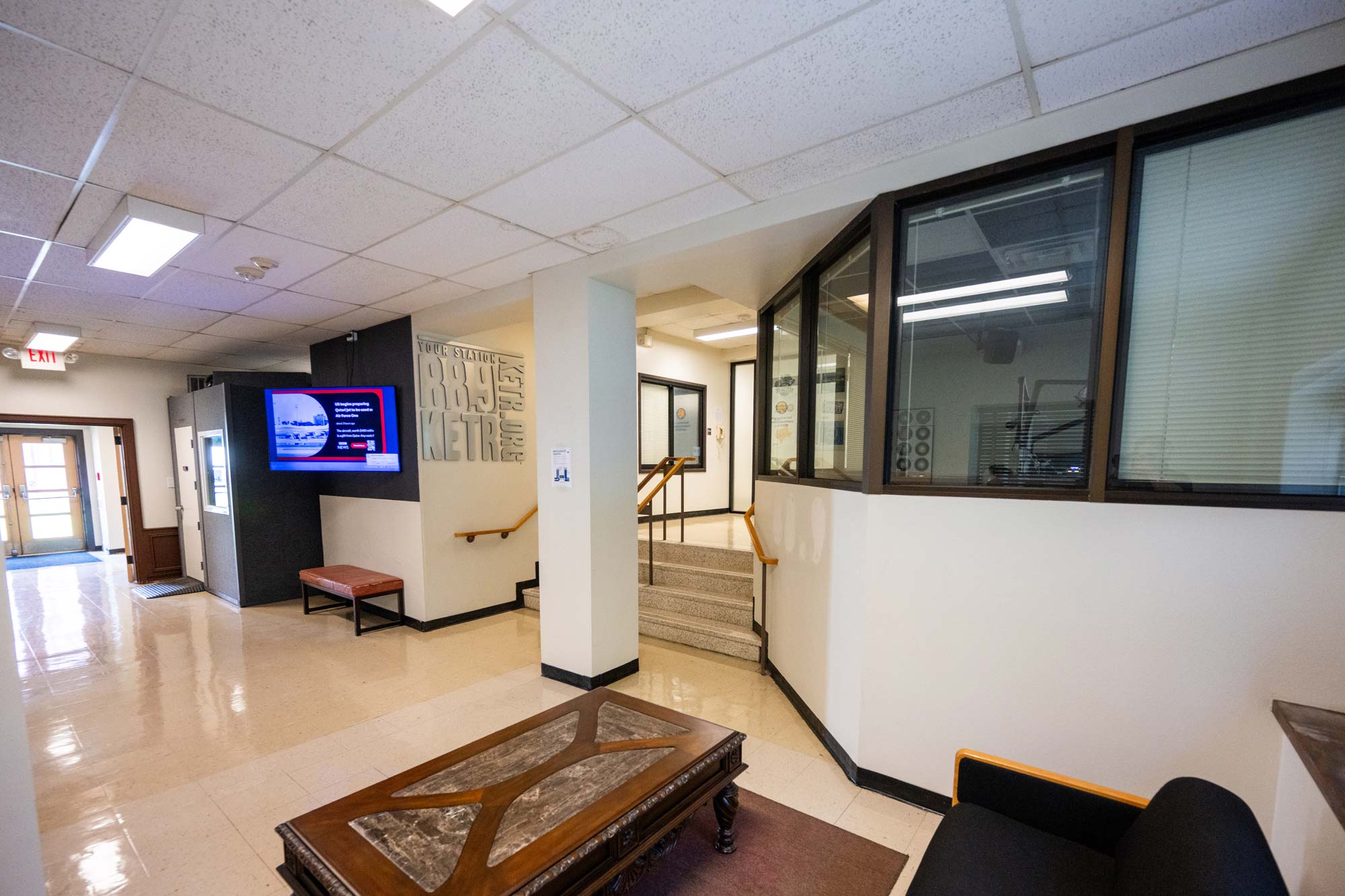 Interior of a building with off-white ceilings, walls and floors. Right side of photo shows interior windows looking into the radio station broadcast room.