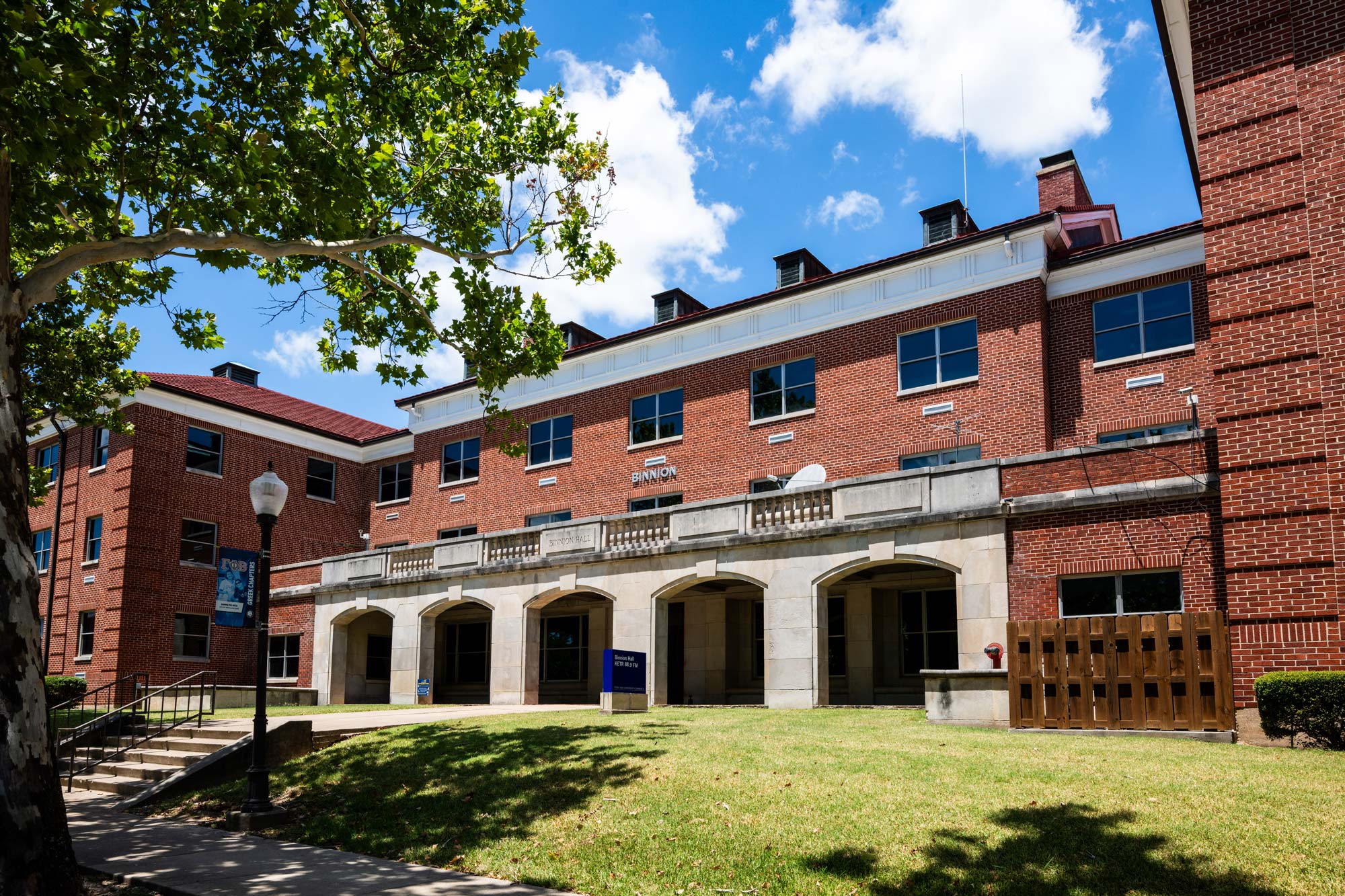 Red, three-story brick building with green grass in front. The front entrance has a porch with arched concrete columns.