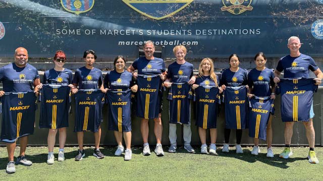 Students and faculty standing in a row, holding up jersey's from a sports team.