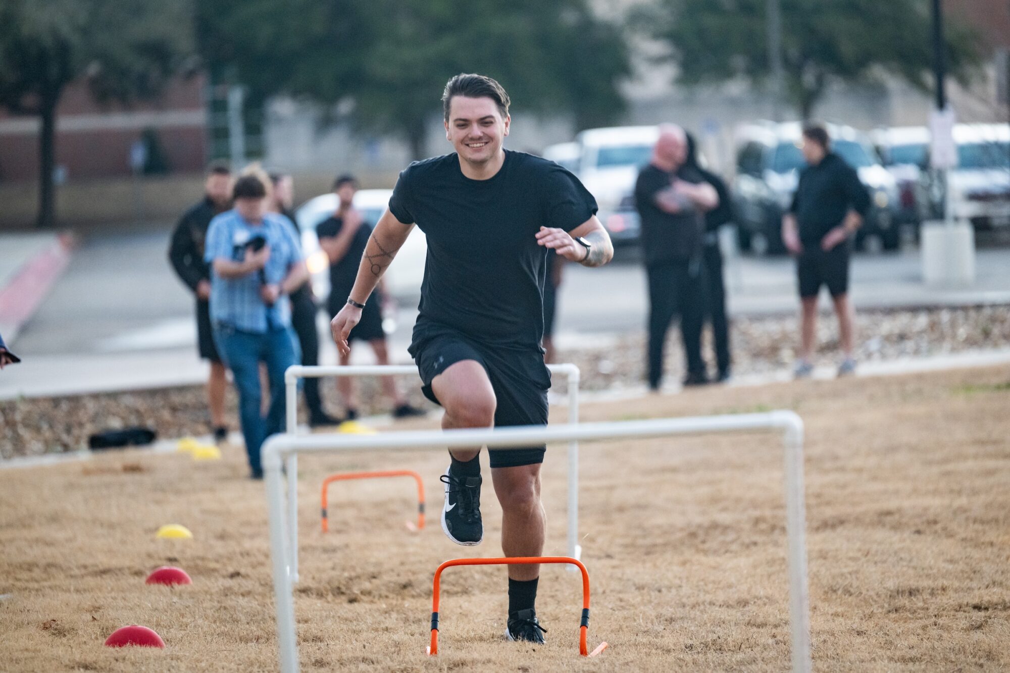 Person jumps over hurdles, toward camera with a smile on his face.