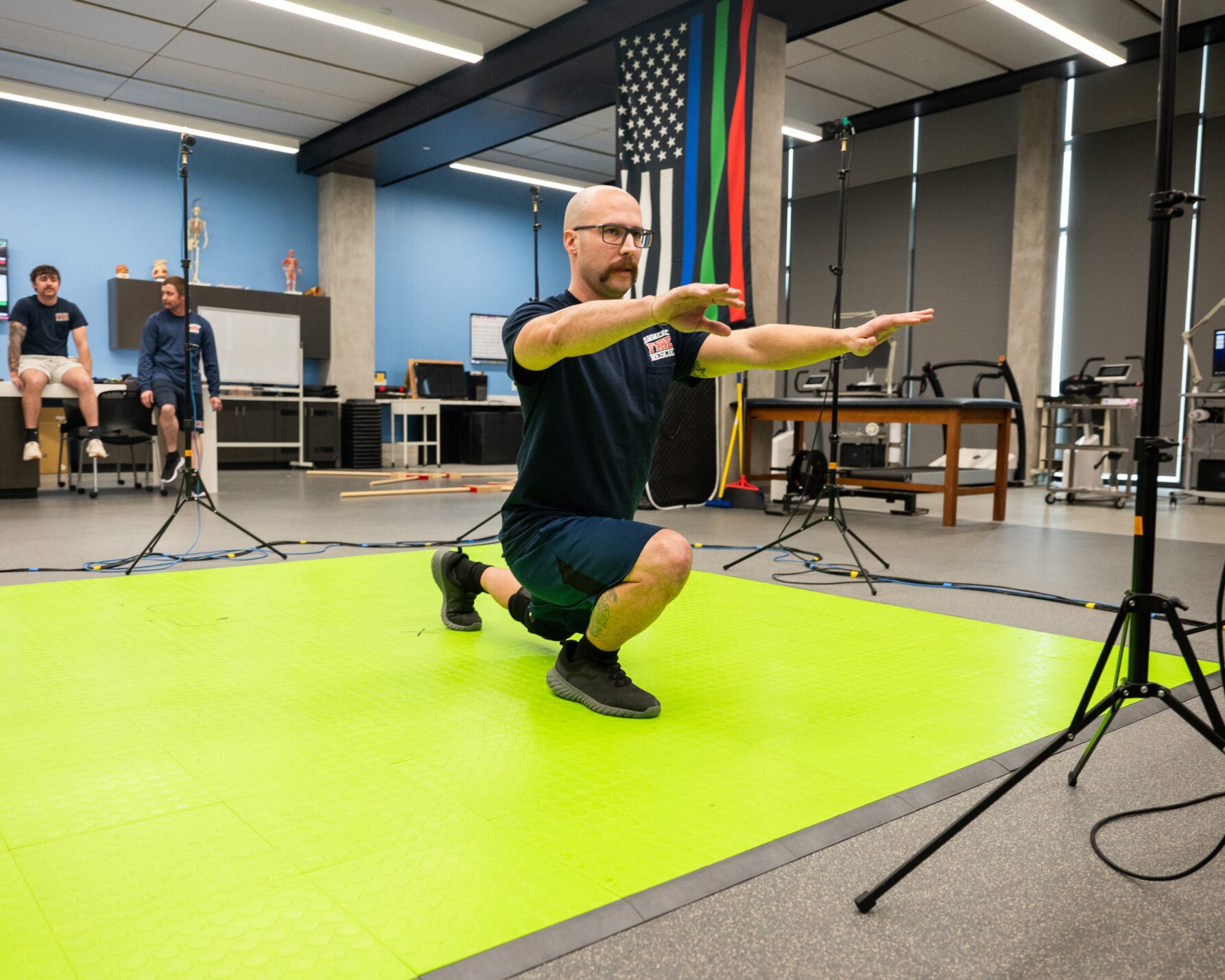 Man in lunge position on a green mat with hands spread straight in front of him. Cameras on tripods are in front and behind him.